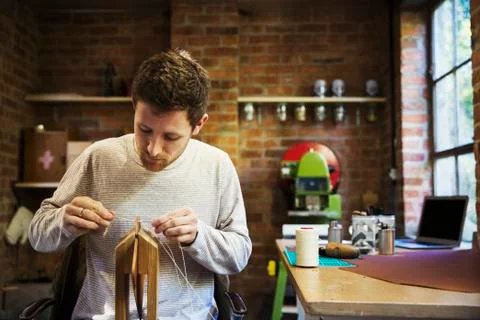 A craftsman seated at a bench in a small workshop, threading string through a Stock Photos