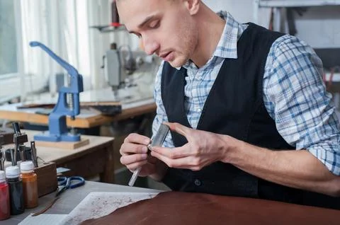 A craftsman sharpens the edge of a leather tool in a workshop Stock Photos