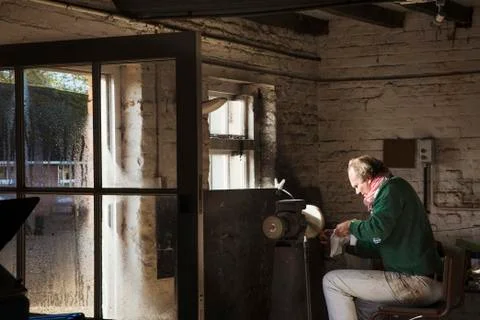 A craftsman sitting in a workshop sharpening the blade of a knife using a 스톡 사진