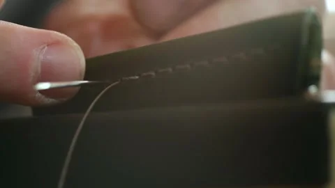 Craftsman skillfully stitching leather with needle and thread in close-up view Stock Footage 296749740