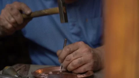 Craftsman strikes patterns on copper vessels with a hammer in his hand Vídeo Stock 329392876