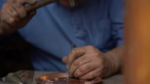 Craftsman strikes patterns on copper vessels with a hammer in his hand Stock Footage 329392880