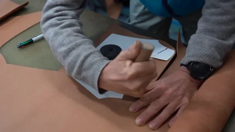 Craftsman tracing a paper shoe pattern onto a large piece of tanned hide before Stock Footage 346297257