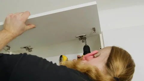 Craftsman uses screwdriver to fix hinge on cabinet door Stock Footage 316188296