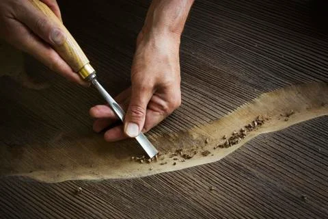 A craftsman using a chisel to carve out a deep groove in a piece of wood. Stock Photos