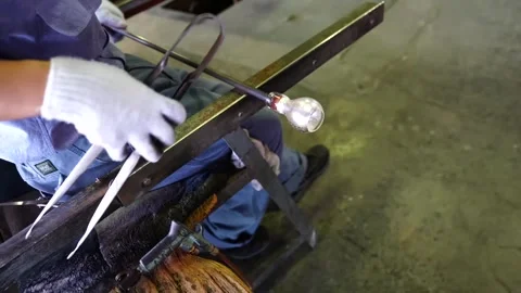 Craftsman using metal jacks to sculpt a glowing glass bubble mounted on a steel Stock Footage 343884331