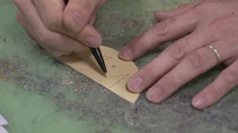 Craftsman using a metal ruler and awl to mark and score a small curved leather Stock Footage 340277519