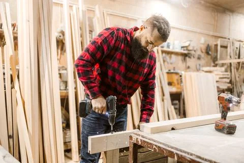 Craftsman using a power drill to work on wooden boards in a workshop during the Stock Photos