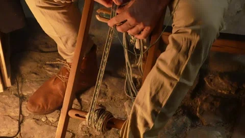 A craftsman weaves a traditional patterned fabric belt on an antique loom. Stock Footage 344440320