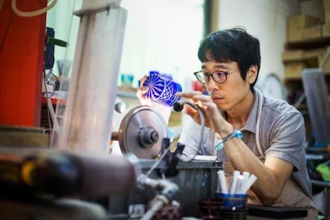 A craftsman at work in a glass maker's workshop polishing a vivid blue cut glass Stock Photos