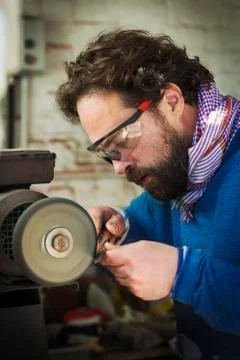 A craftsman at work sharpening the blade of a knife using a surface grinder 스톡 사진