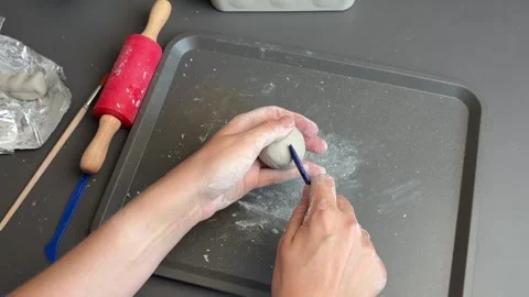 Craftsperson adding deep grooves to a hand formed clay pumpkin on a studio tray Stock Footage 345719910