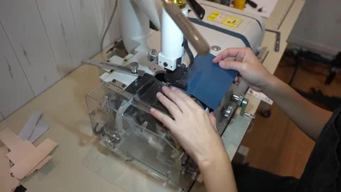 Craftsperson feeds blue leather panel through sewing machine presser foot Stock Footage 339642822