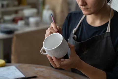 Craftswoman makes sketch of future pattern on white mug to decorate kitchen with Stock-Fotos