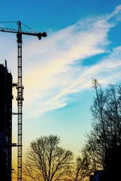 Crane attached to the building against the backdrop of sunset and trees Stock Photos
