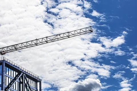 A crane for construction work against a blue sky with wavy clouds. Real Est.. Stock Photos