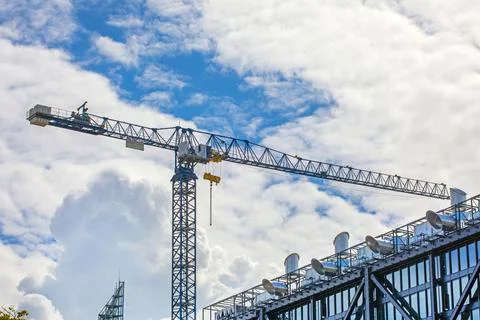 A crane for construction work against a blue sky with wavy clouds. Real Est.. Stock Photos