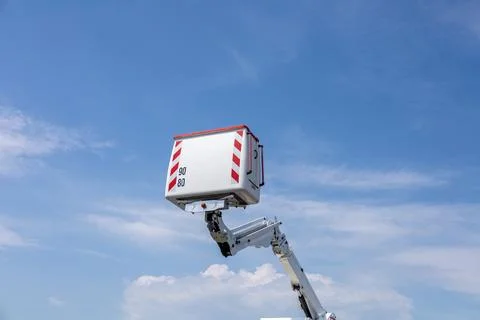 A crane extends its arm, lifting a cargo box toward the clouds on a sunny d.. Stock Photos