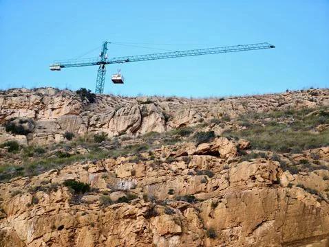 Crane hoists load over ridge, Heavy machinery raises cargo over rocky lands.. Stock Photos