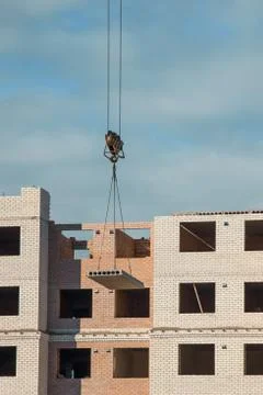 Crane lifting cement block on the background of building under construction. Stock Photos
