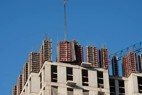 Crane lifting formwork on building construction site against blue sky Stock Photos