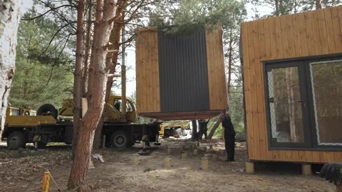 Crane Lifting Modern Prefab Cabin Into Place in Wooded Area Stock Footage 277643401