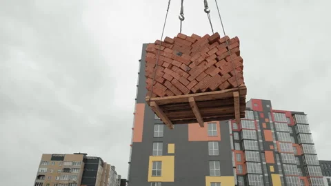 Crane lifting a pallet of bricks at a construction site, A pallet of red bricks Stock Footage 302750999