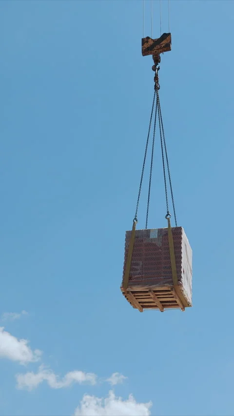 Crane lifting pallet of bricks at construction site, A crane lifting a pallet of Stock Footage 310312639