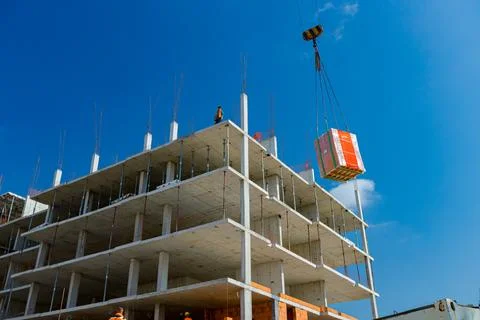 Crane is lifting pile red blocks packed in plastic foil on unfinished, buil.. Stock Photos
