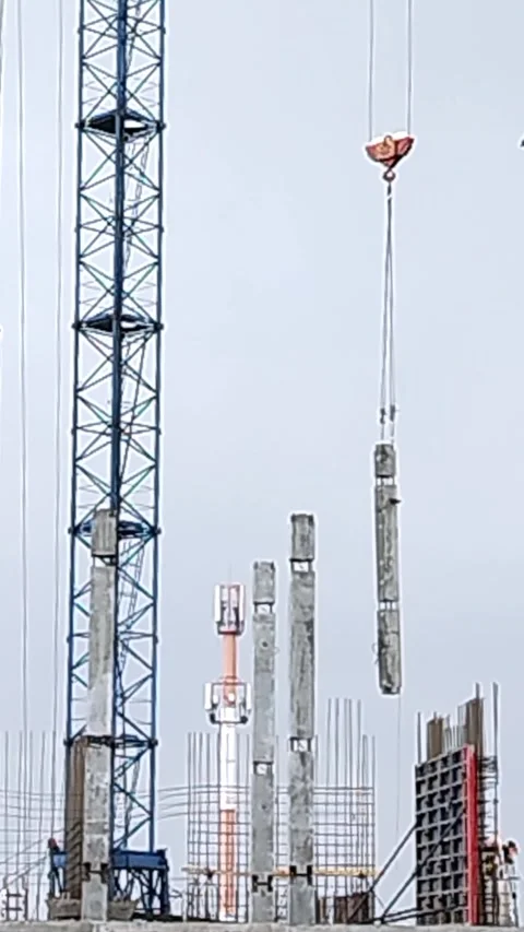 Crane lifts concrete column at construction site with workers and scaffolding in Stock Footage 340606685