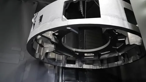 Crane lowering a large cast aluminum wheel hub into position at a foundry Stock Footage 343370663