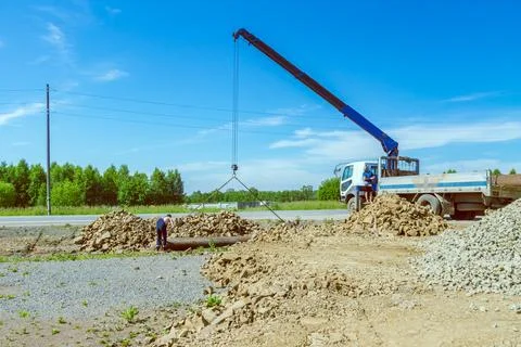 Crane lowering large pipe into roadside drainage trench under clear sky Stock Photos