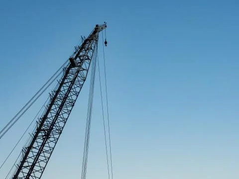 Crane machinery covered in shadows in a cloudless late evening sky Stock Photos