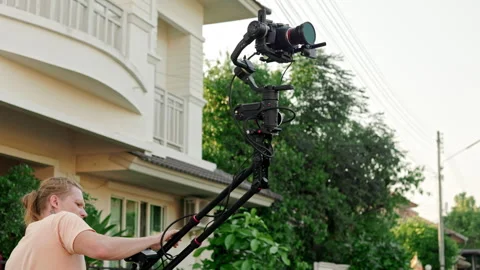 A crane-mounted camera is being used by a cameraman to film outside, with a Stock Footage 244738061