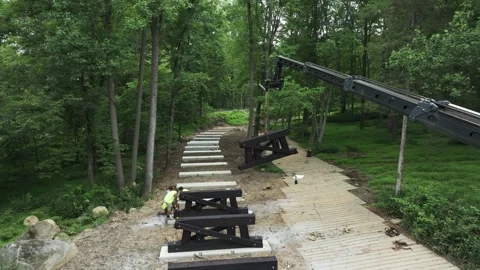 A crane moves along a narrow path in a forest setting. Workers set up equipment Видео 331270847