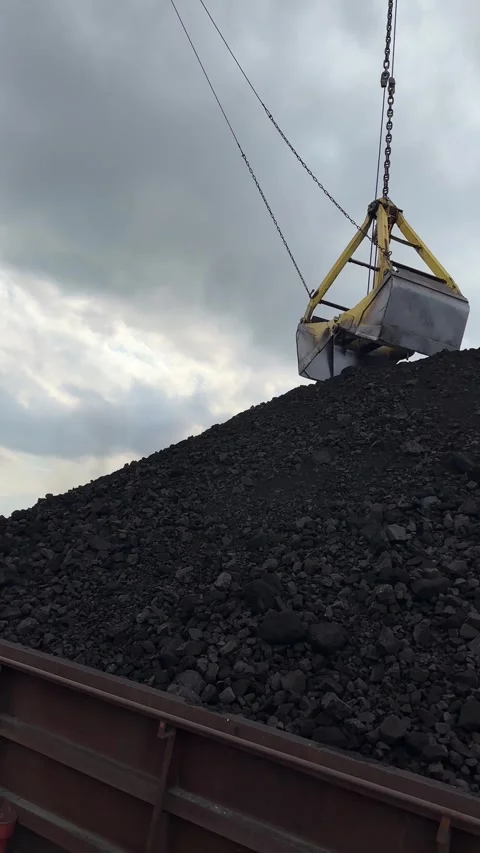 Crane operating with a bucket to load coal from a large pile onto a delivery Stock Footage 309466767