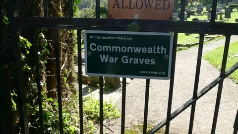 Crane pan shot of Commonwealth war graves sign on metal gates, grave yard behind Vídeo Stock 118353747