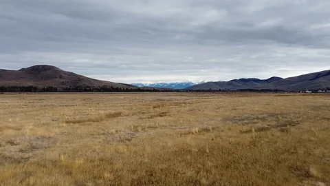 Crane shot of wide open grass field with rolling hills and snow capped mounta Stock Footage 125050654