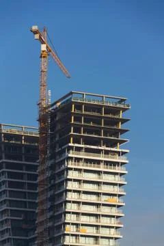 Crane on skyscraper construction site with windows reflecting sky 写真素材