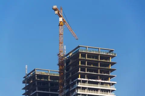 Crane on skyscraper construction site with windows reflecting sky 写真素材