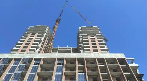 Cranes and construction of a high multi-storey building, house against the blue Stock Photos
