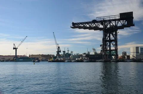 Cranes and shipyard structures reflecting on calm waters under blue sky Foto stock