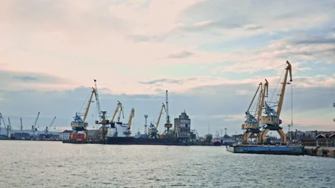 Cranes move cargo at a busy dock during early evening hours along the waterfront Stock Footage 331085616