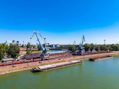 Cranes work to load coal from a dock onto barges along a river. This scene sh Stock Photos