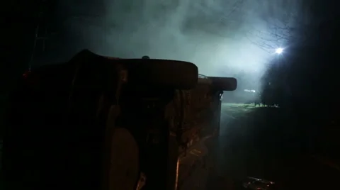 Crashed car on its side at night with light through trees Stock Footage 58642663