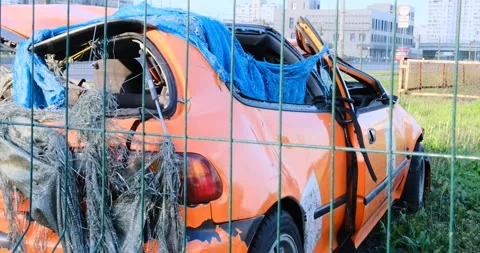 A crashed orange car with a dented body and roof sits abandoned in the grass Stock Footage 274770857