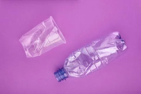 Crashed plastic bottle and cup on purple background. Plastic utilisation concept Stock Photos