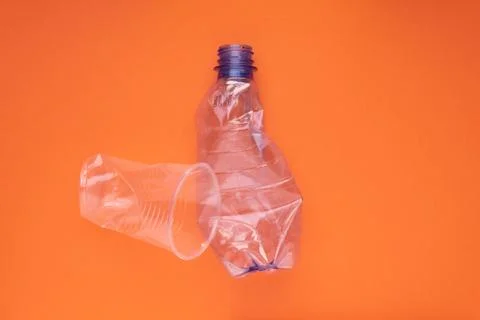 Crashed plastic bottle and cup on orange background. Plastic utilisation concept Stock Photos