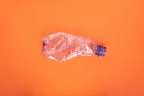 Crashed plastic bottle on orange background. Plastic utilisation concept Stock Photos