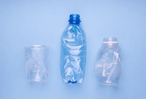 Crashed plastic bottles and a cup on bright blue background. Plastic utilisation Stock Photos